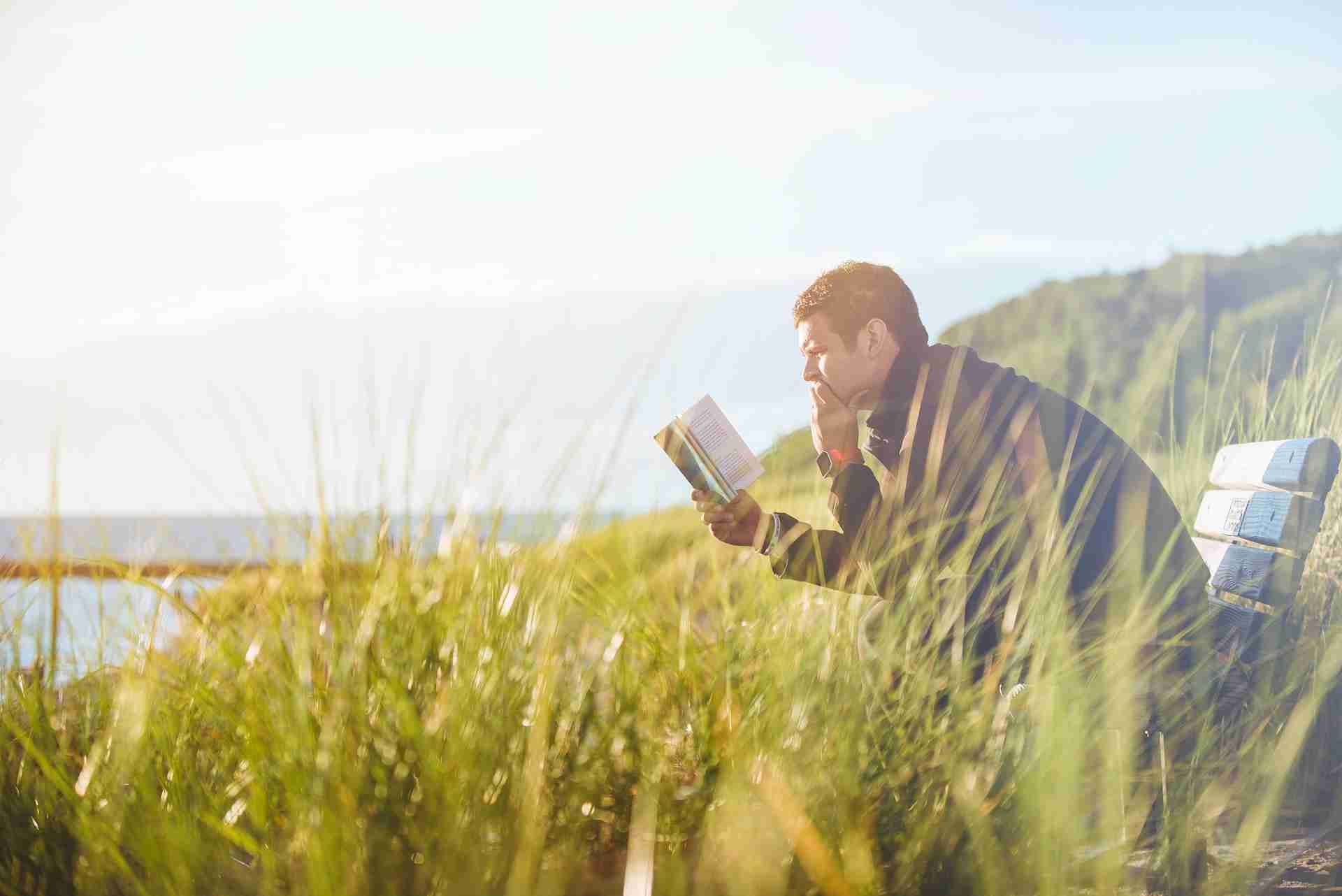 Ein Mann sitzt auf einer Bank und ließt konzentriert ein Buch.