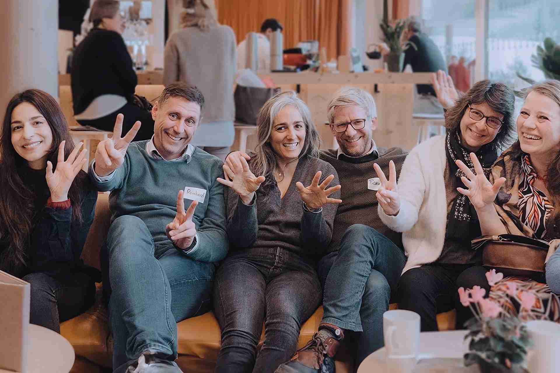 Gruppenbild lachende Teilnehmer:innen MIO-Tage die die Hände in die Kamera halten und sich austauschen zu Resilienz