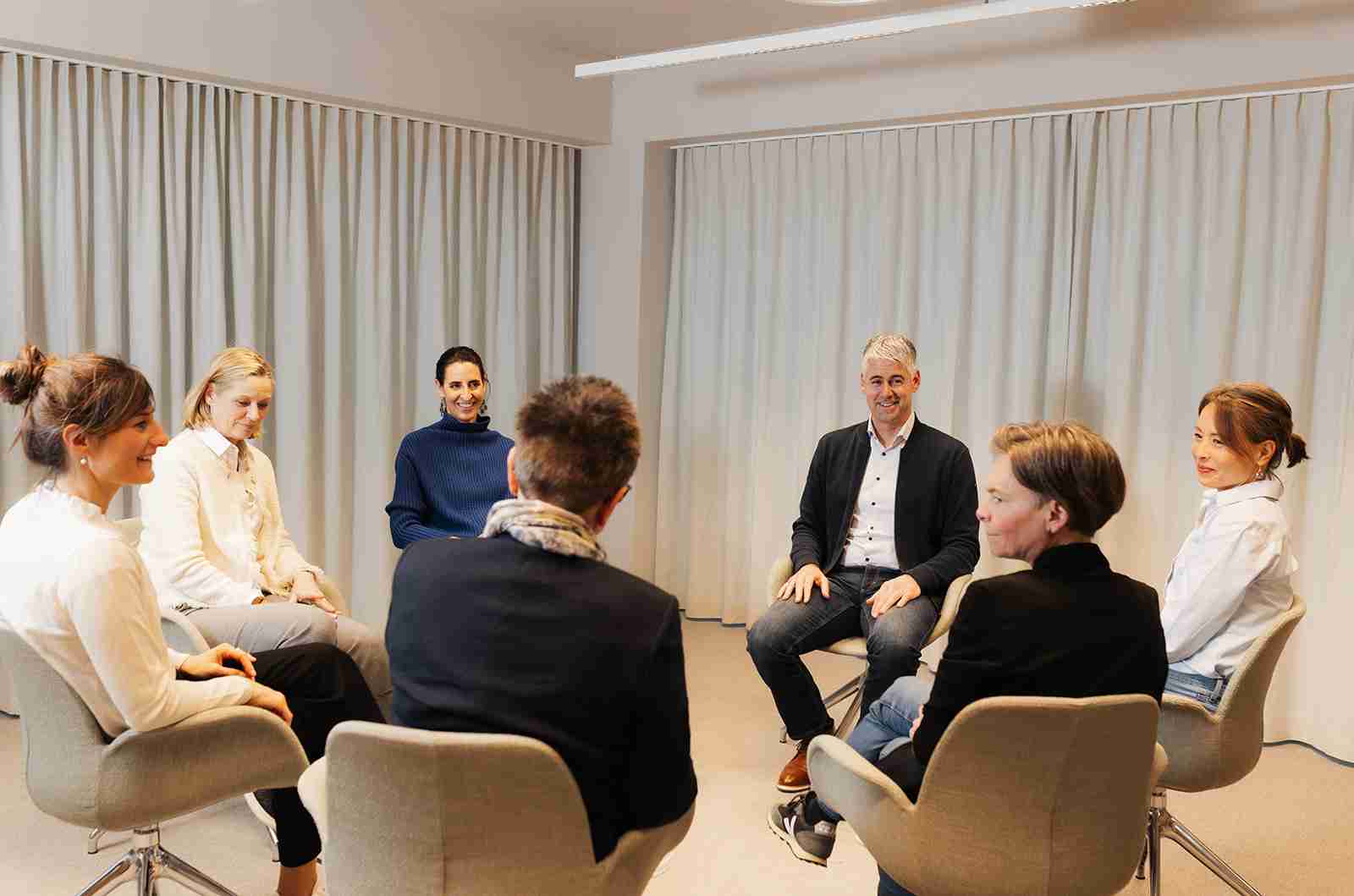 Führungskraft lachend im Kreis sitzend mit grauen Haaren